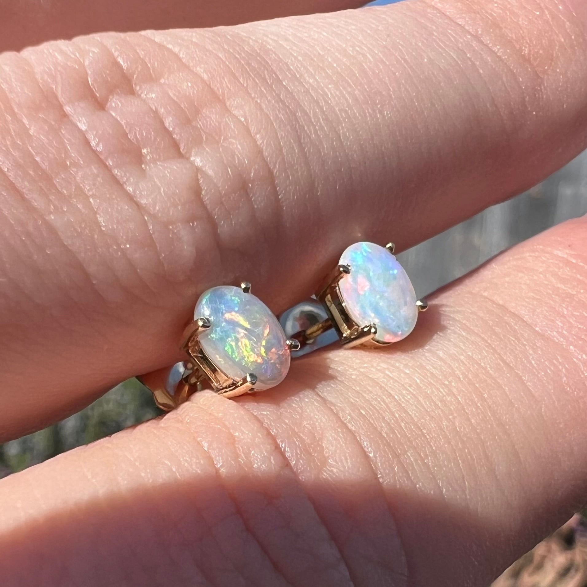 Angled view of opal stud earrings in sunlight, showing an orange flash.