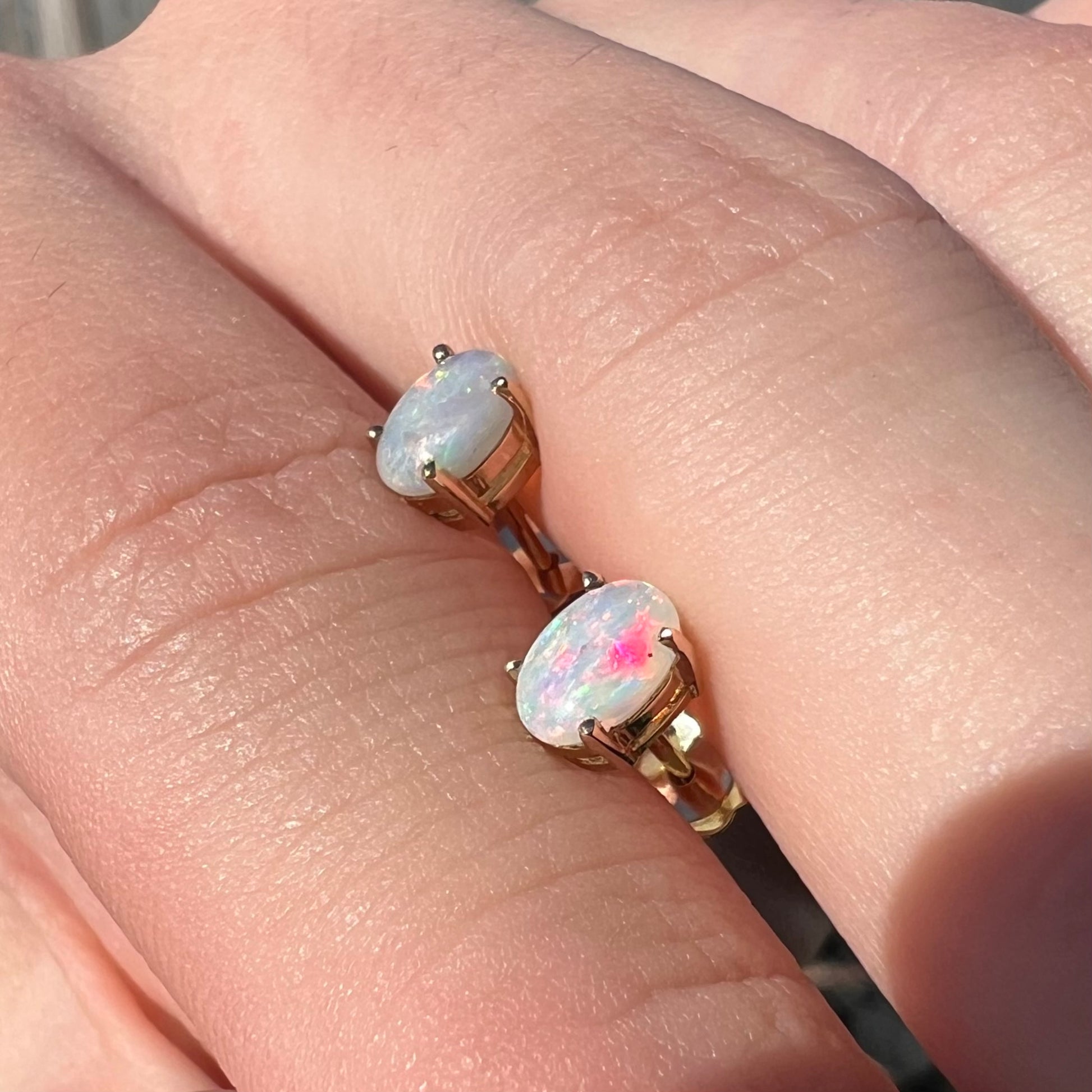 A different angled view of opal stud earrings in sunlight, revealing a strong pink fire.