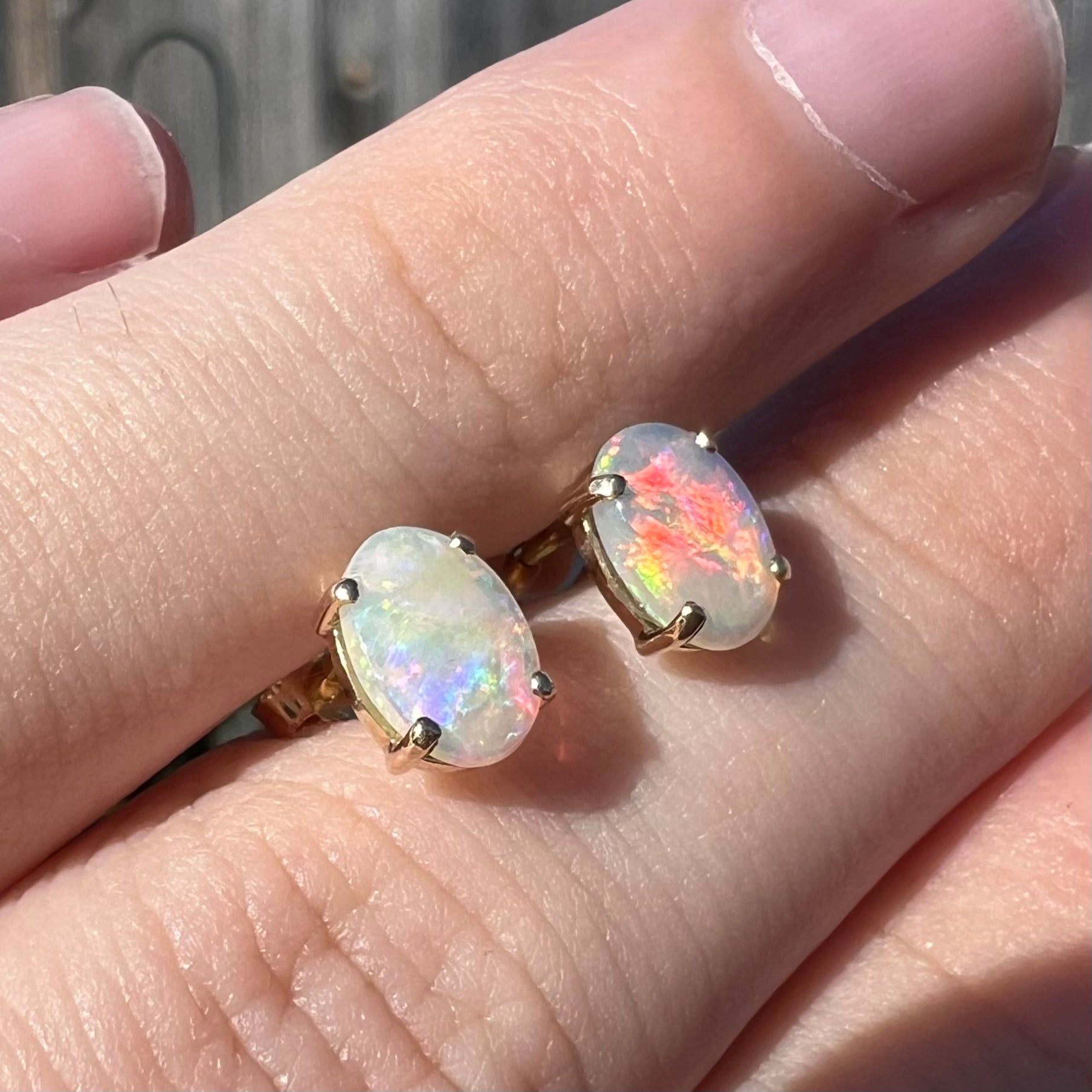 Angled view of opal stud earrings in sunlight, with one opal showing a striking red flash.