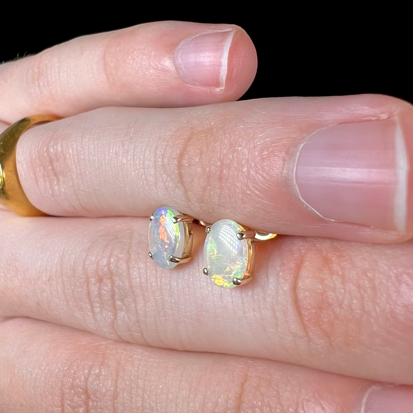 Opal stud earrings viewed at a different angle, one opal showing subtle green fire while the other displays a red flash.