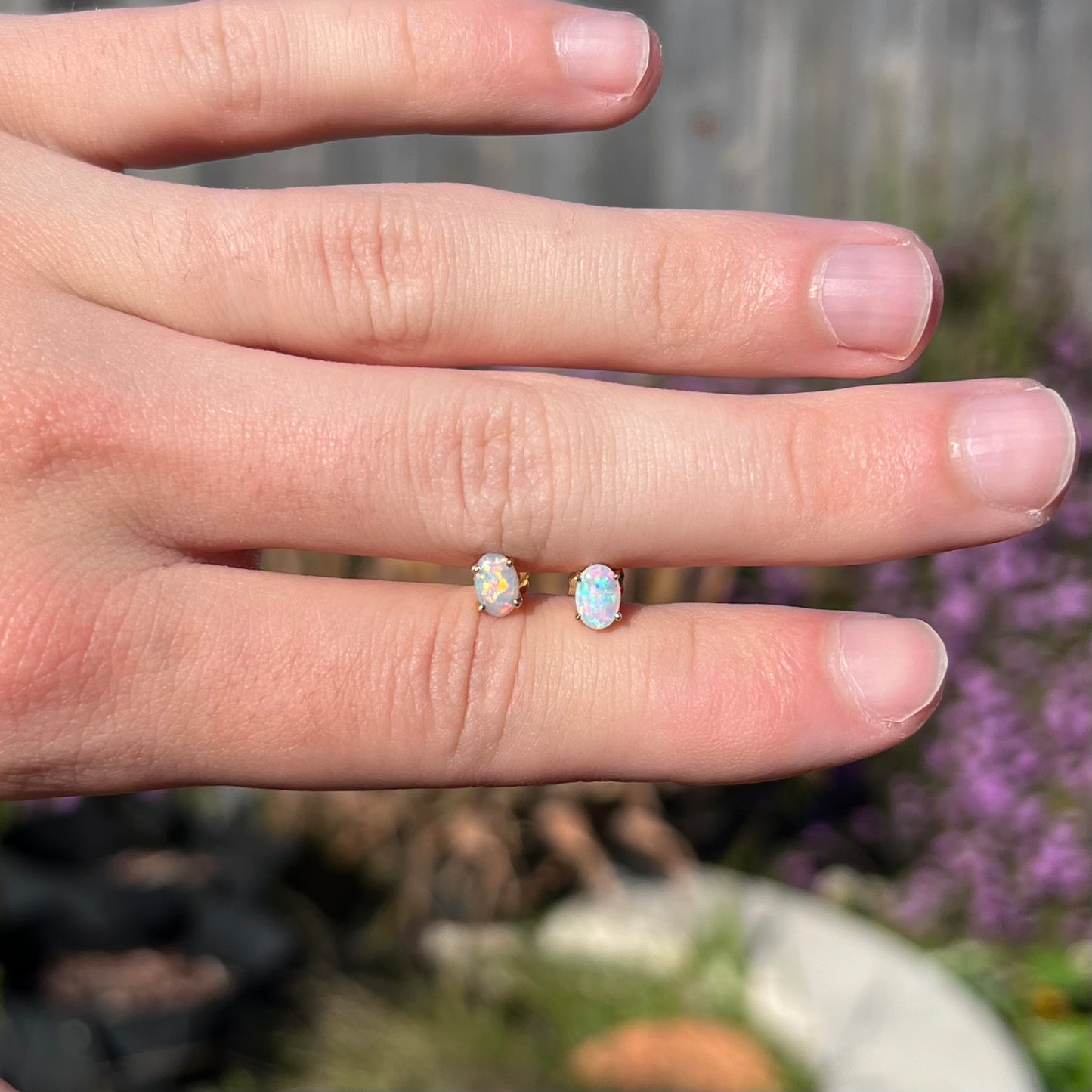 Opal stud earrings held in hand outdoors in natural sunlight, colors appearing vibrant.