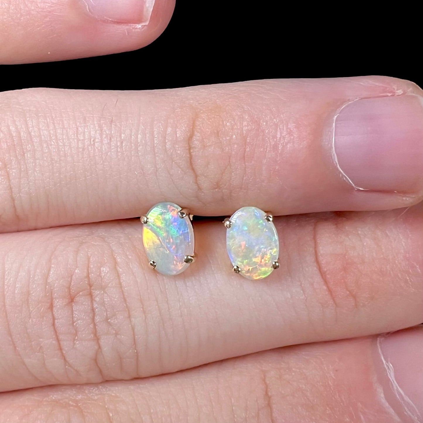 A macro close-up of opal stud earrings, showing multicolor flashes of red, green, and yellow.