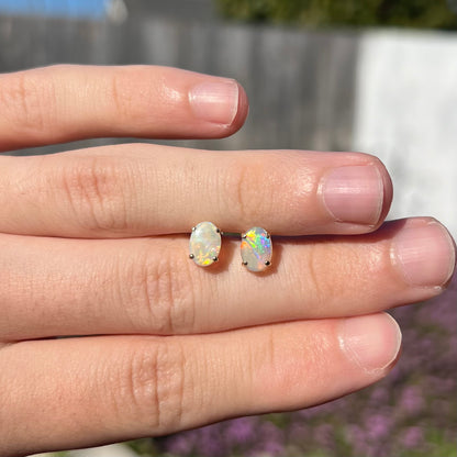 Opal stud earrings held in hand outdoors in natural sunlight, with one opal showing vibrant color play.