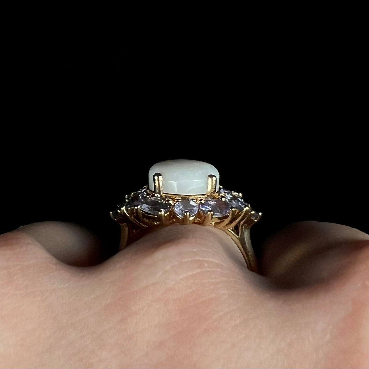 Side profile gallery view of an Australian white opal and tanzanite cluster ring, worn on hand; the ring's prongs are in view