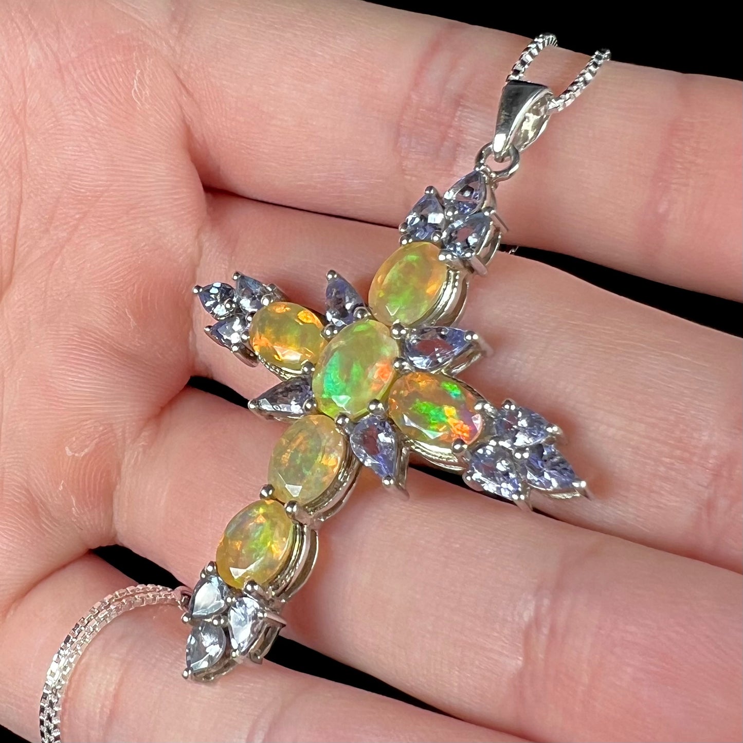 An opal and tanzanite cross necklace shown at a close-up angled view.