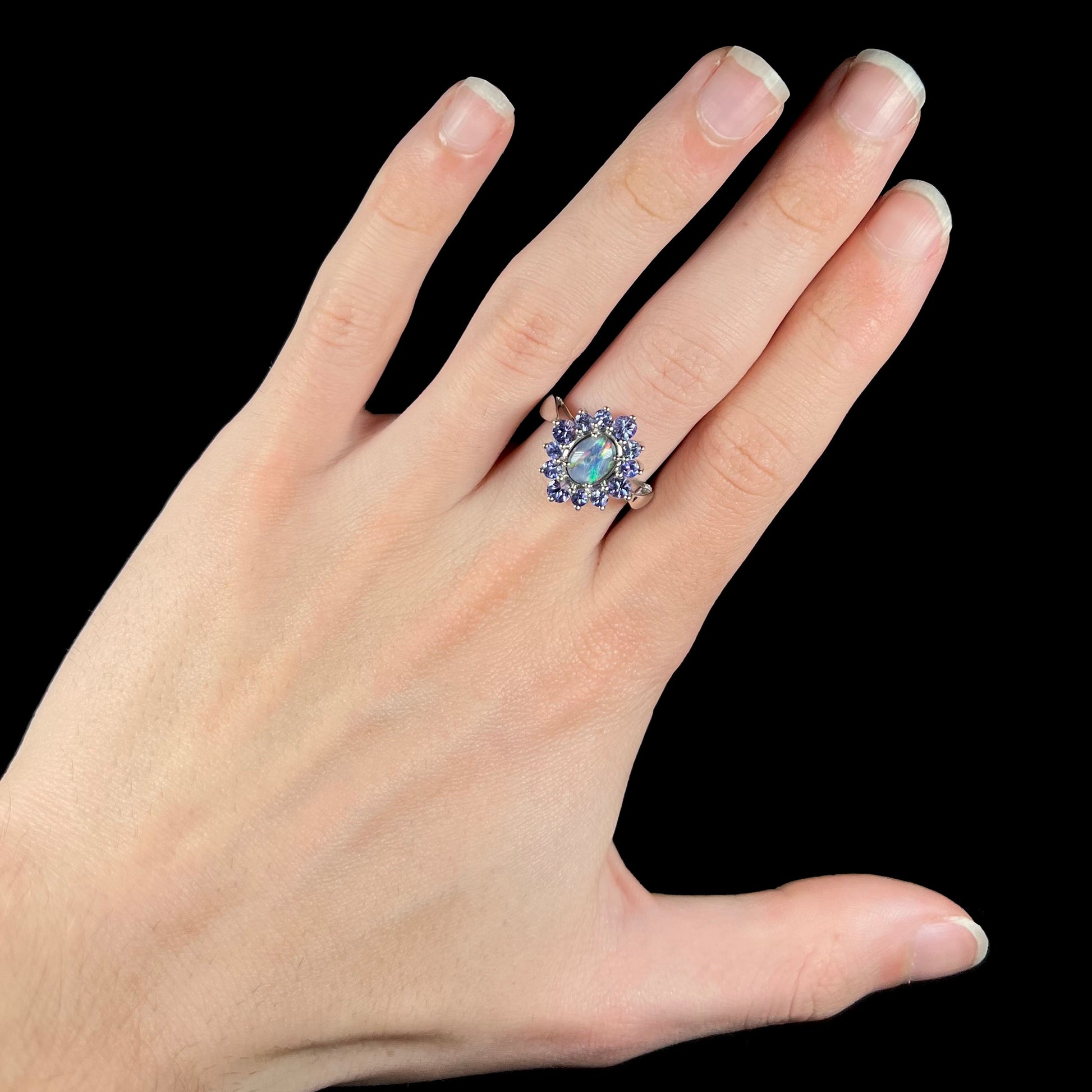 A hand wearing a black opal triplet and tanzanite halo ring.