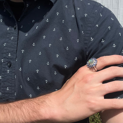 A hand resting on an opposing arm while wearing an opal and tanzanite ring in harsh natural light.