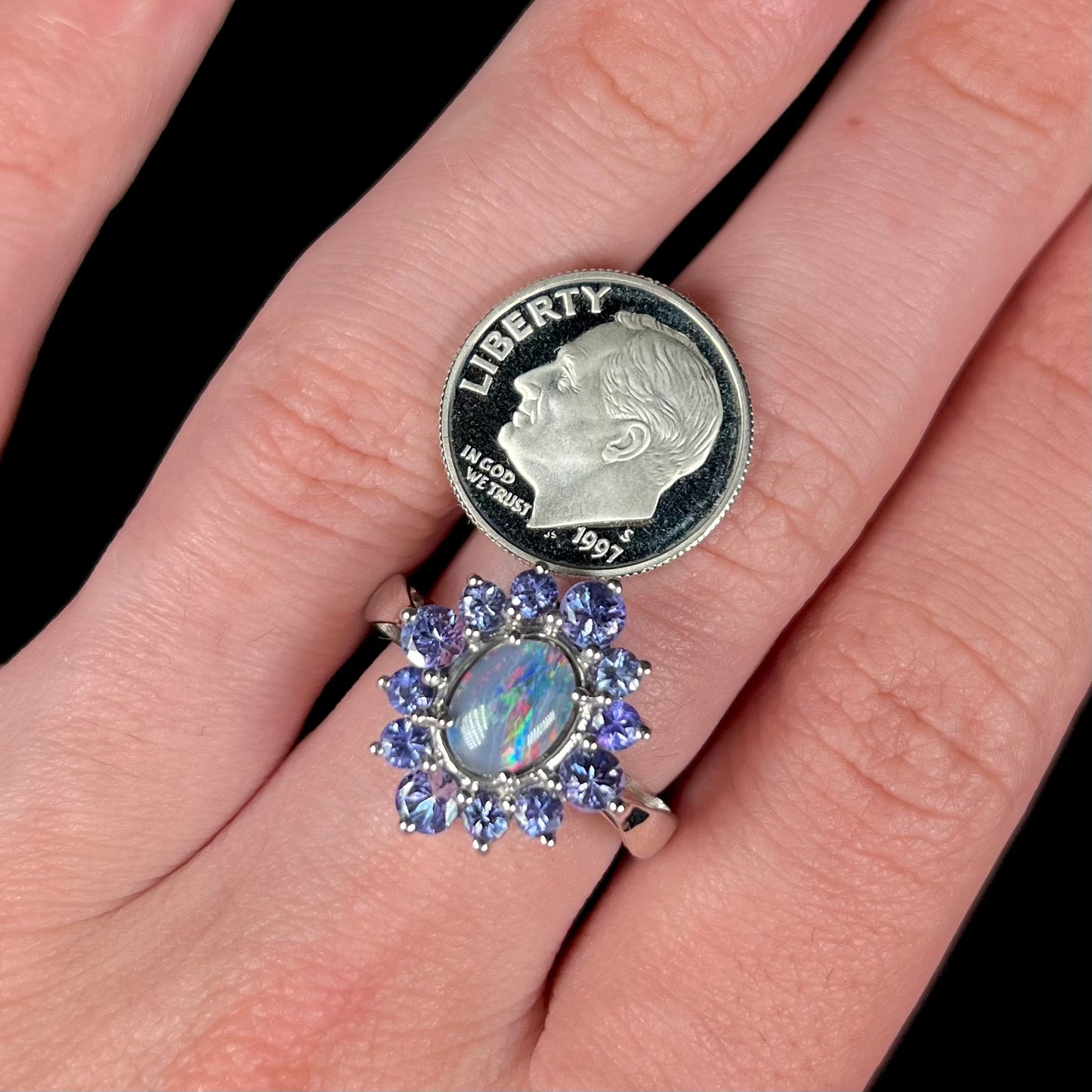 A silver black opal tanzanite halo ring worn on a hand, next to a US dime coin.