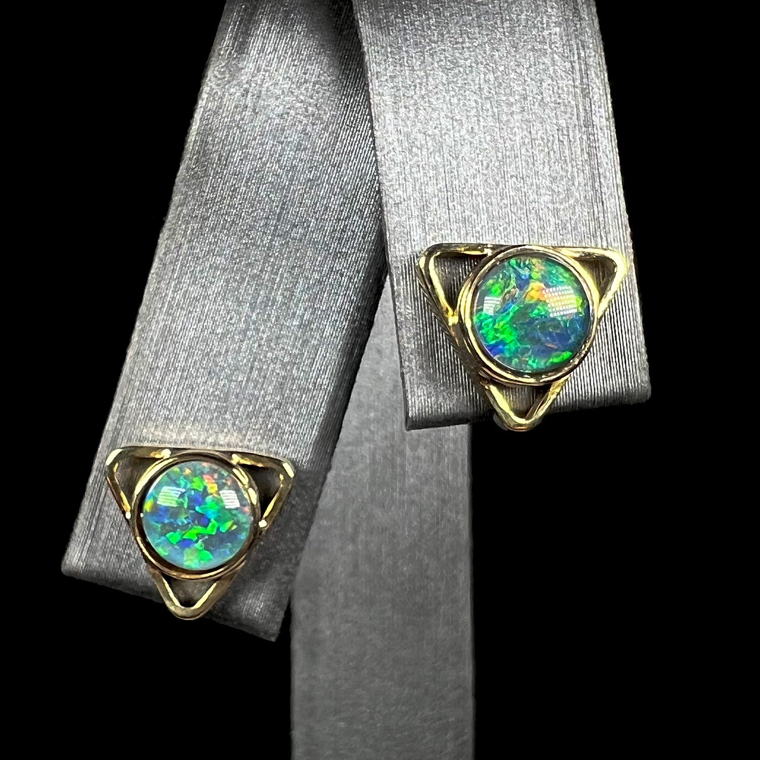 A pair of triangle shaped 18k yellow gold opal stud earrings, shown from the front view.