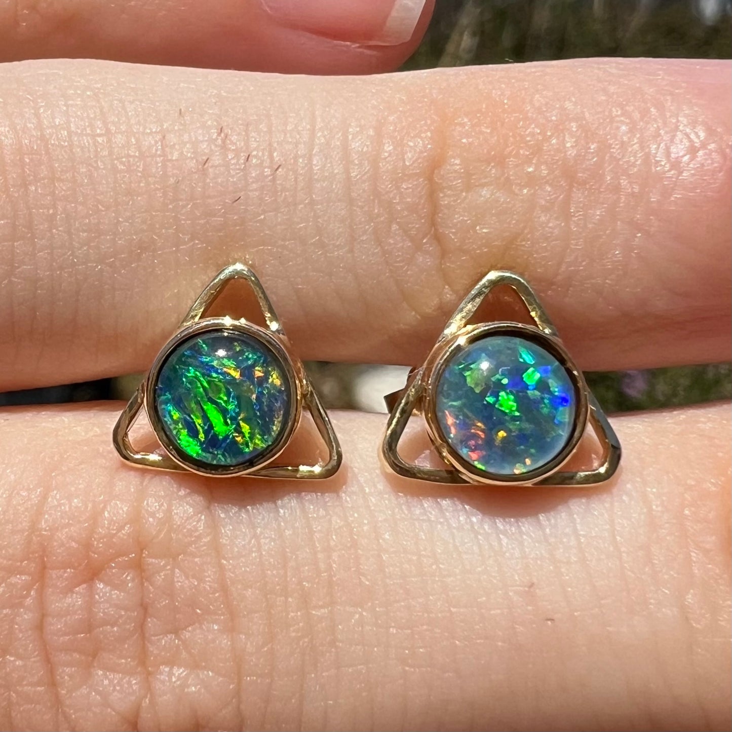 Close-up front view of a pair of opal triangle earrings shown in the sunlight.  The opals have green fire.