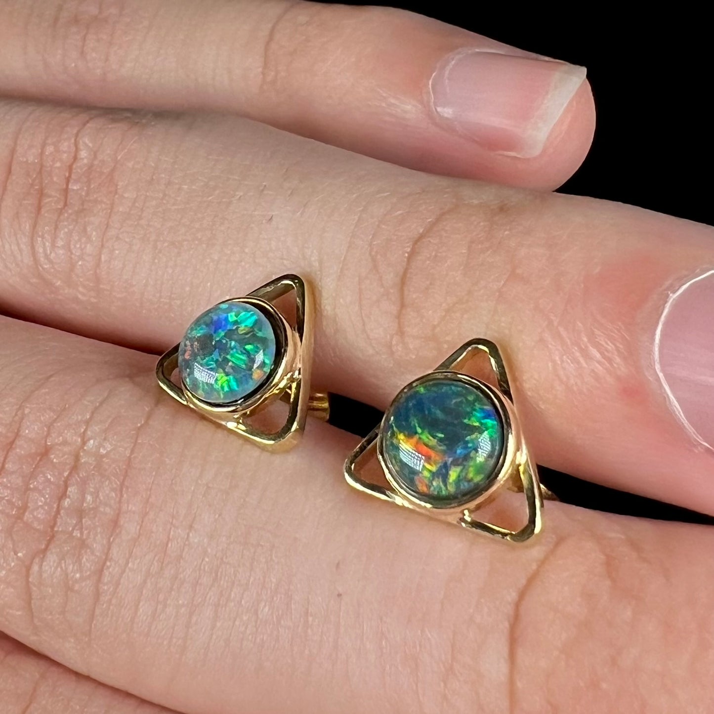 Close-up angled view of a pair of opal triangle stud earrings, resting on top of a hand.