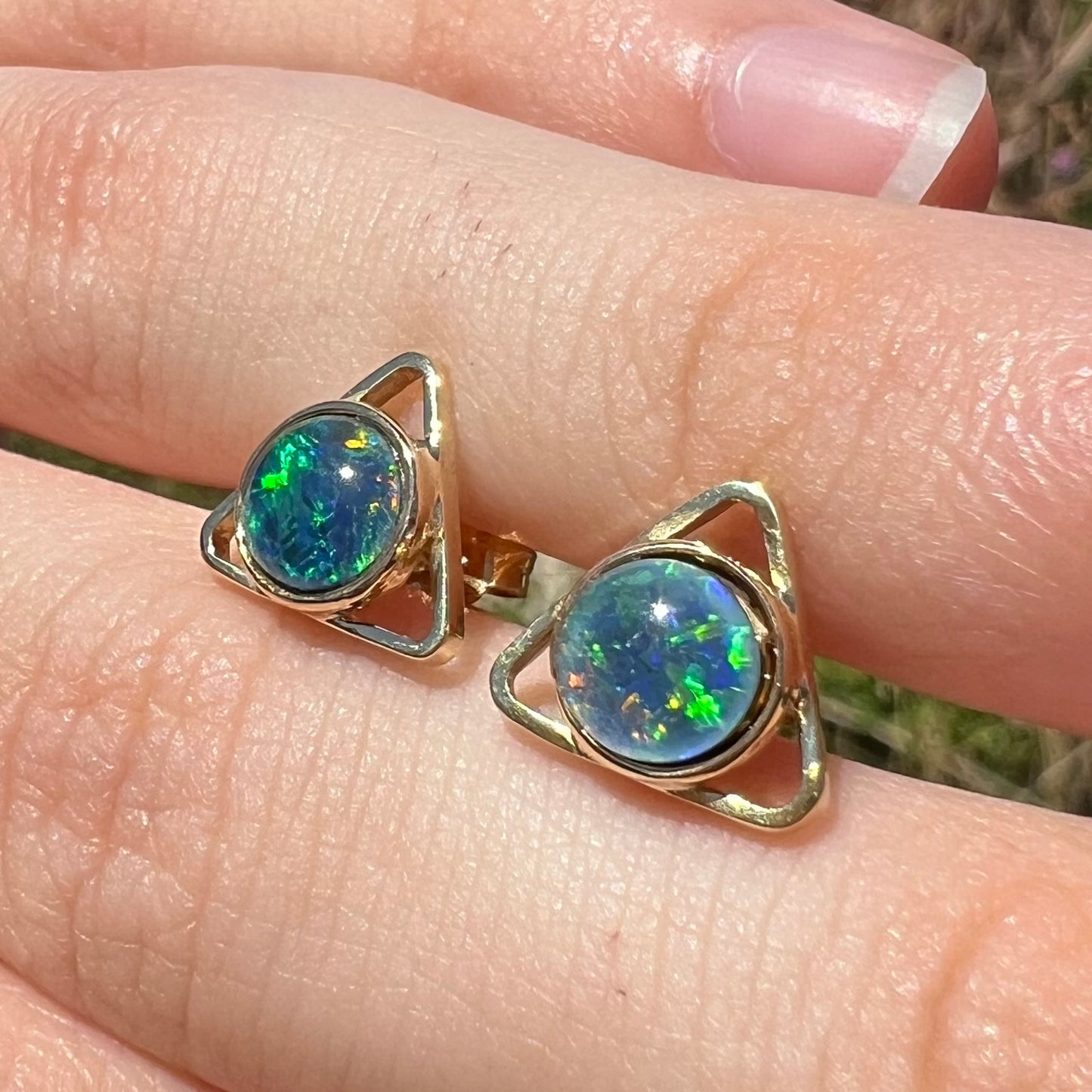 A pair of opal triangle stud earrings shown at an angle in the sunlight on top of a hand.