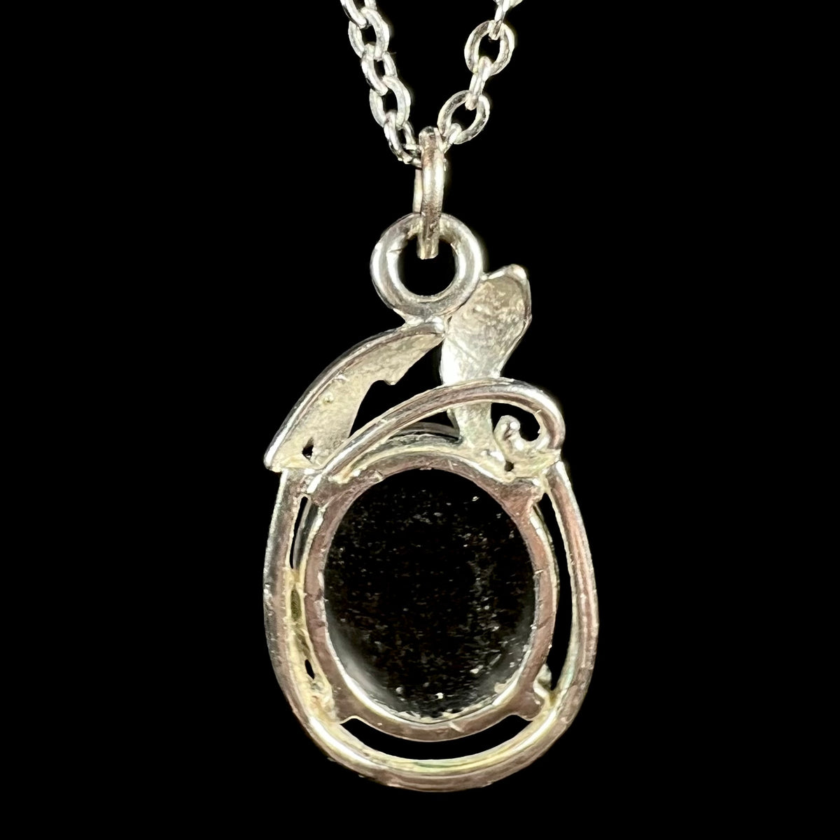 Back side of base metal opal triplet pendant on chain; the pendant's open back shows opal's black backing