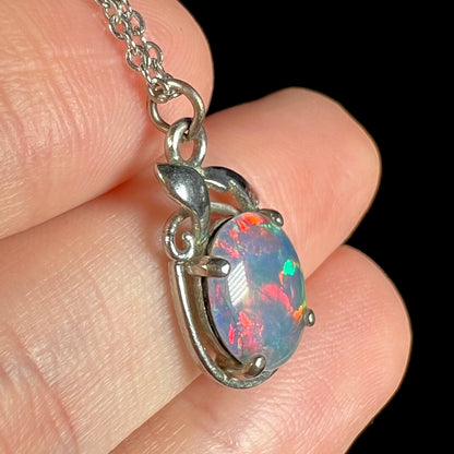 Side view of opal triplet pendant with red and green flashes of color, shown close-up in hand