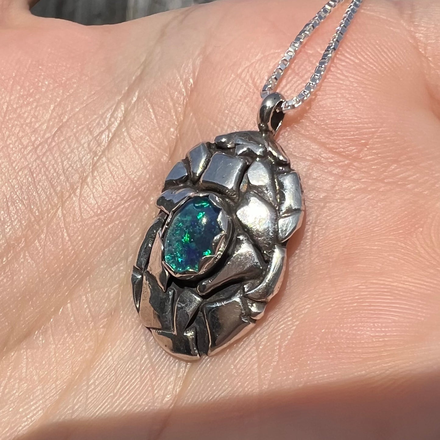 A unisex sterling silver pinecone-inspired opal triplet necklace shown in the sunlight from an angle.