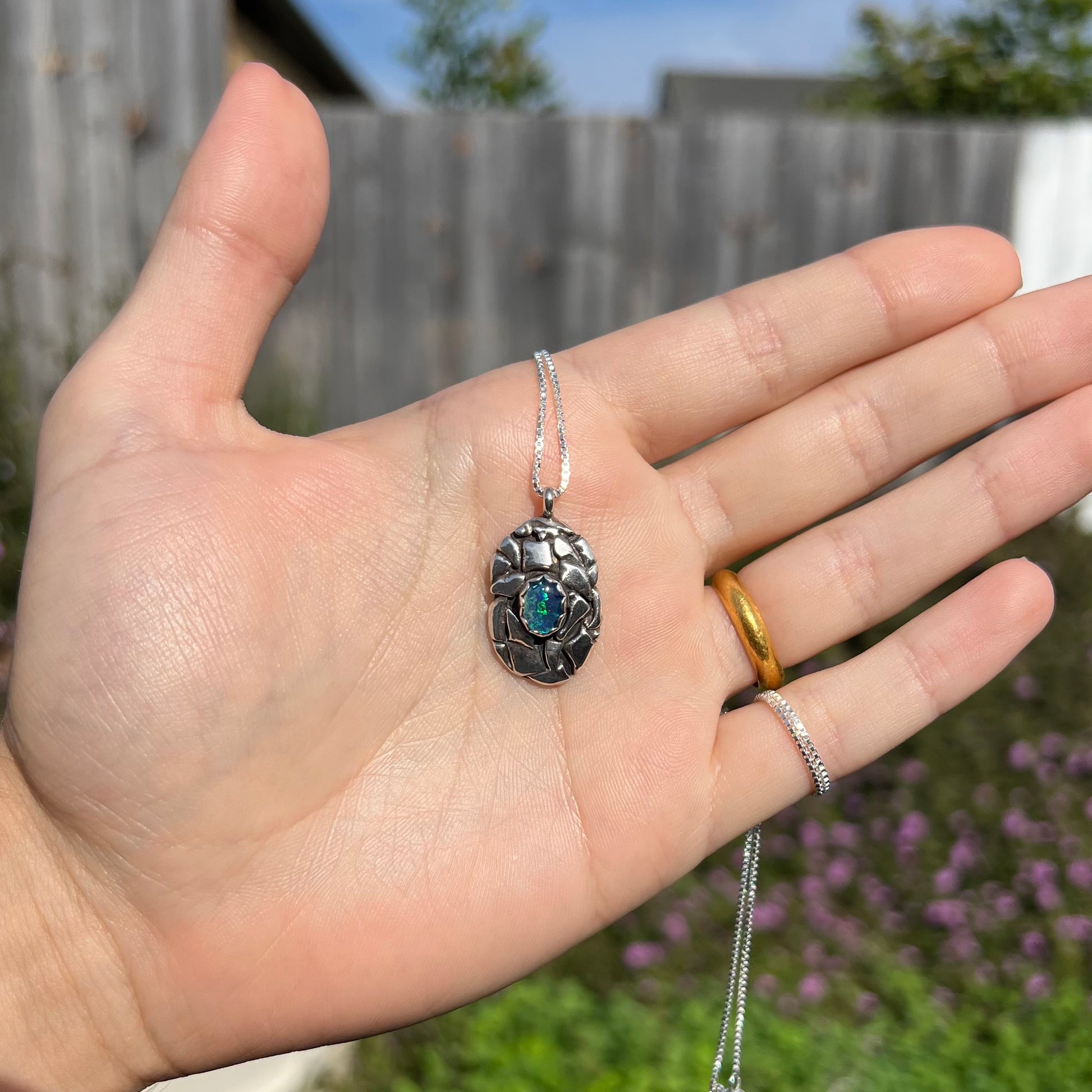 A unisex sterling silver pinecone-inspired opal triplet necklace shown in a hand in sunlight.