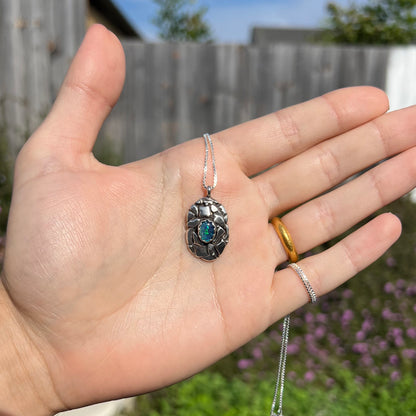 A unisex sterling silver pinecone-inspired opal triplet necklace shown in a hand in sunlight.