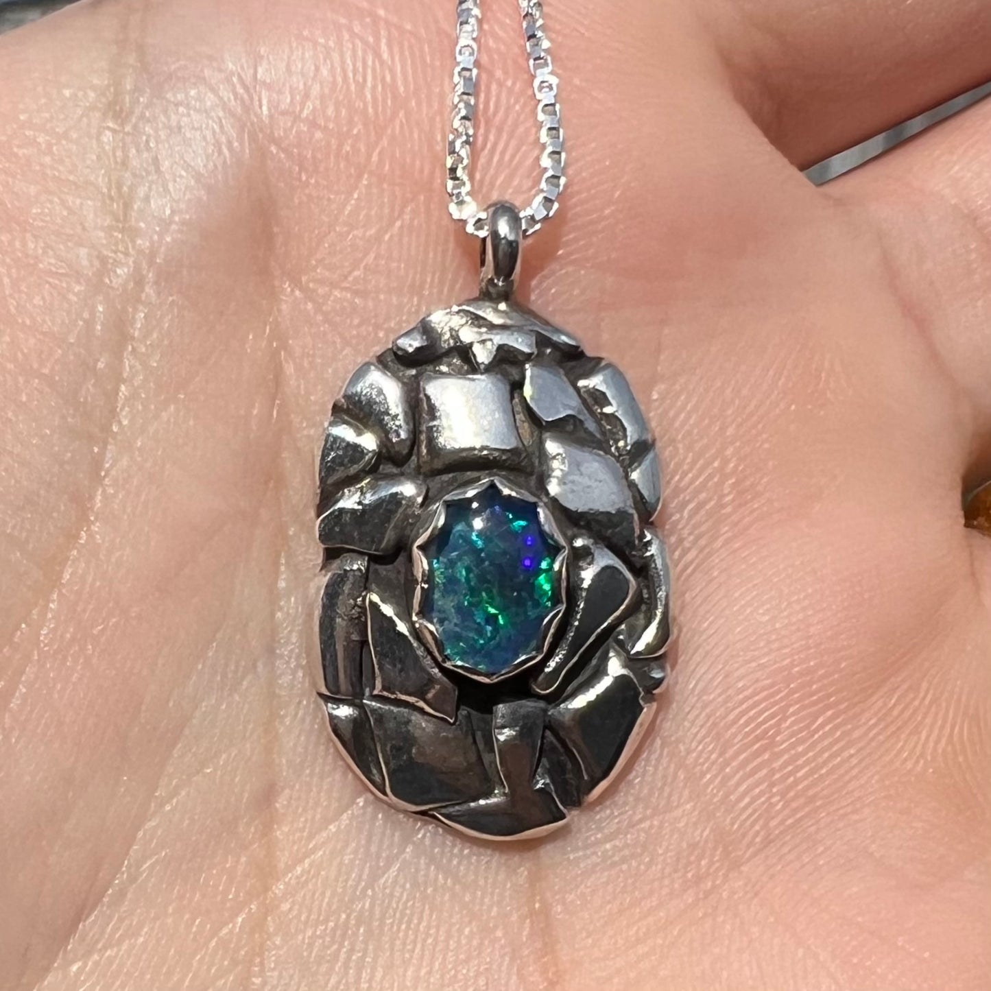 A unisex sterling silver pinecone-inspired opal triplet necklace shown in the sunlight.