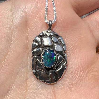 A unisex sterling silver pinecone-inspired opal triplet necklace shown in the sunlight.