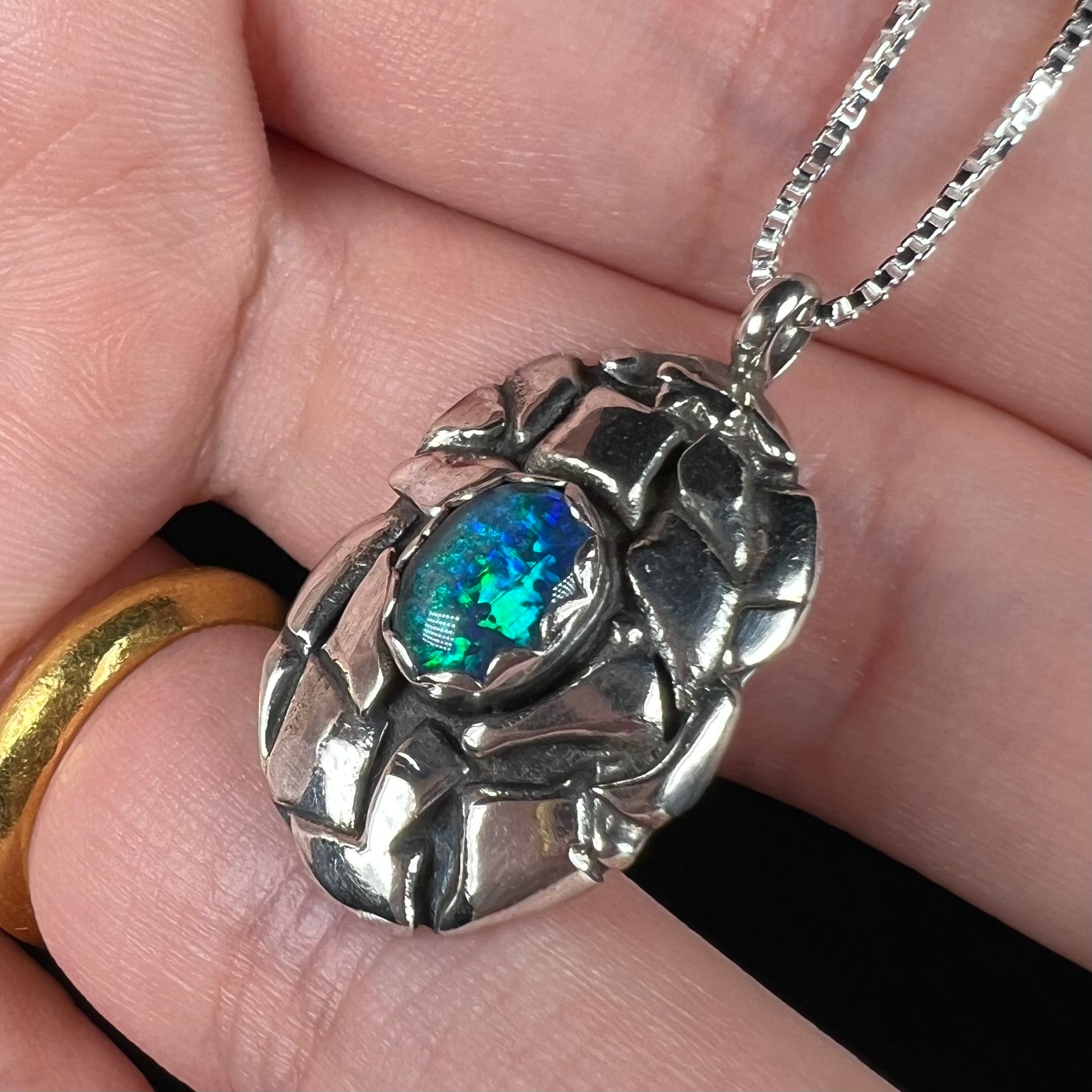 A unisex sterling silver pinecone-inspired opal triplet necklace with blue color play.
