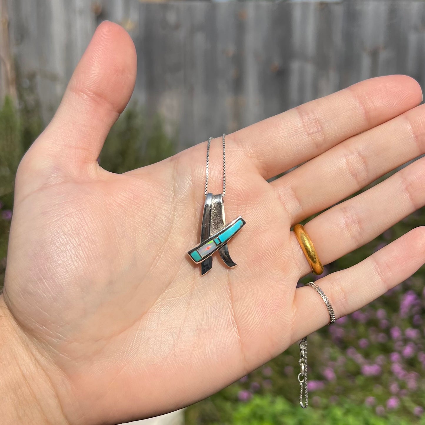 A folded design sterling silver turquoise and lab-created opal inlay necklace shown in the sunlight in a hand.