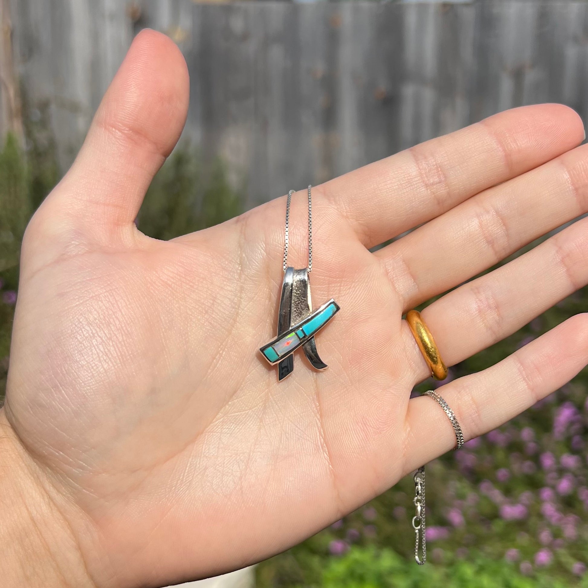 A folded design sterling silver turquoise and lab-created opal inlay necklace shown in the sunlight in a hand.
