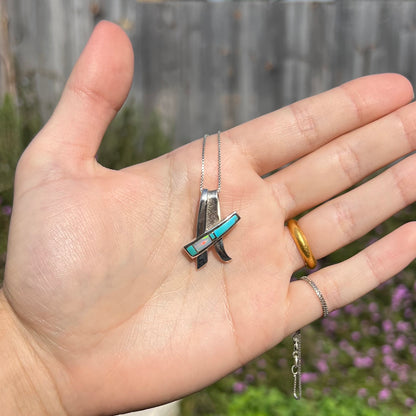 A folded design sterling silver turquoise and lab-created opal inlay necklace shown in the sunlight in a hand.
