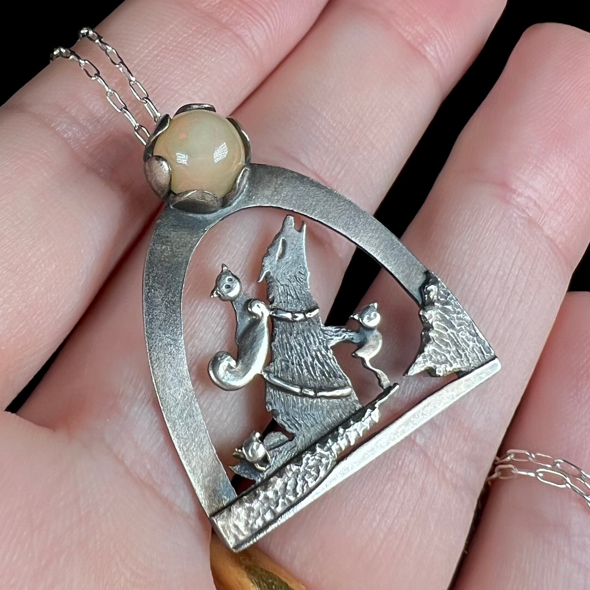 Close-up angled view of a sterling silver Ethiopian opal wolf and cat design necklace, held in a hand.