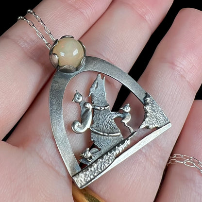 Close-up angled view of a sterling silver Ethiopian opal wolf and cat design necklace, held in a hand.