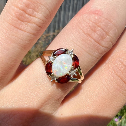 A ladies natural opal ring in yellow gold.  The opal is surrounded by red marquise cut garnets and diamonds.