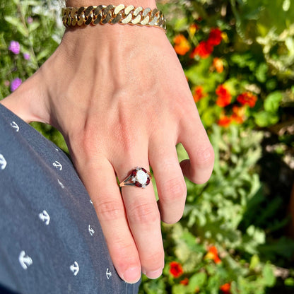 A ladies natural opal ring in yellow gold.  The opal is surrounded by red marquise cut garnets and diamonds.