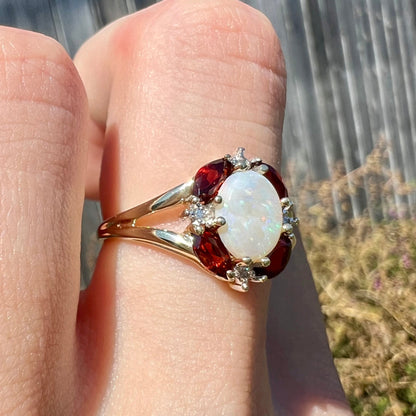 A ladies natural opal ring in yellow gold.  The opal is surrounded by red marquise cut garnets and diamonds.