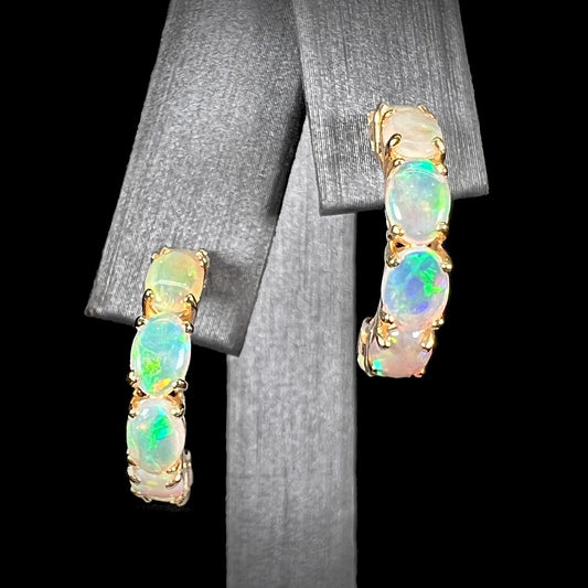 A pair of yellow gold opal hoop earrings.  Each earring is set with six natural oval cut opals.