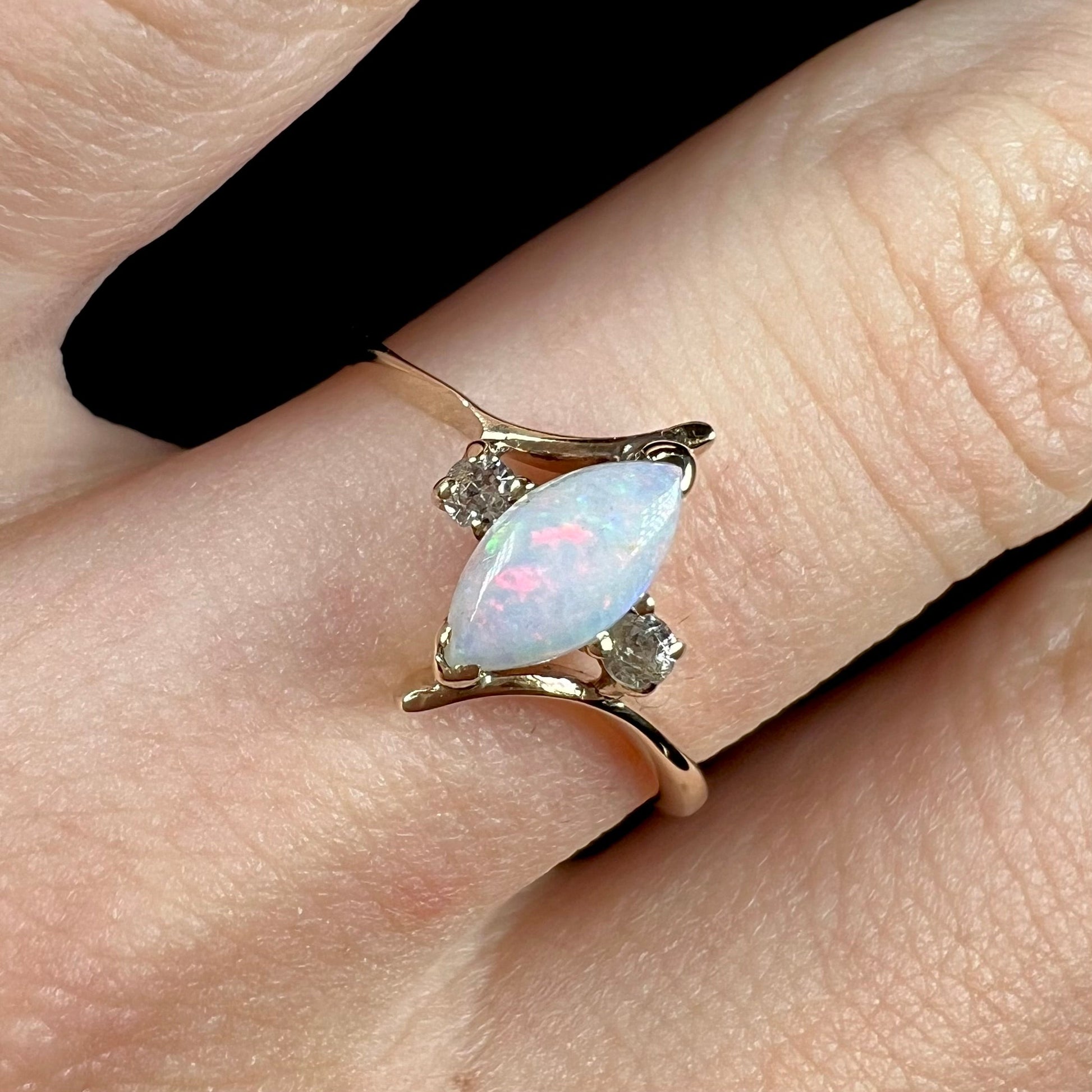 A yellow gold marquise cut opal ring set with two white sapphire accent stones.