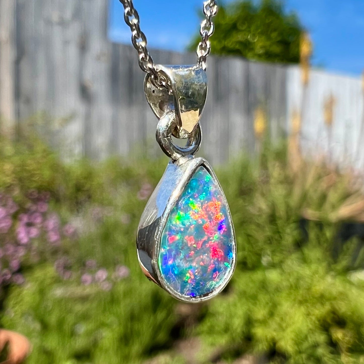 A pear shaped black opal necklace set in sterling silver.  The opal vividly flashes every color of the rainbow.