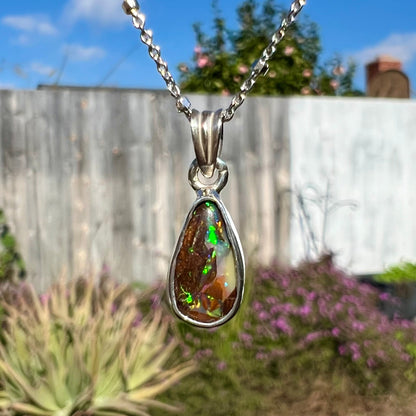 A pear shaped boulder opal necklace in sterling silver.  The opal has bright green and blue flashes.