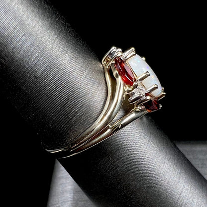 A ladies natural opal ring in yellow gold.  The opal is surrounded by red marquise cut garnets and diamonds.