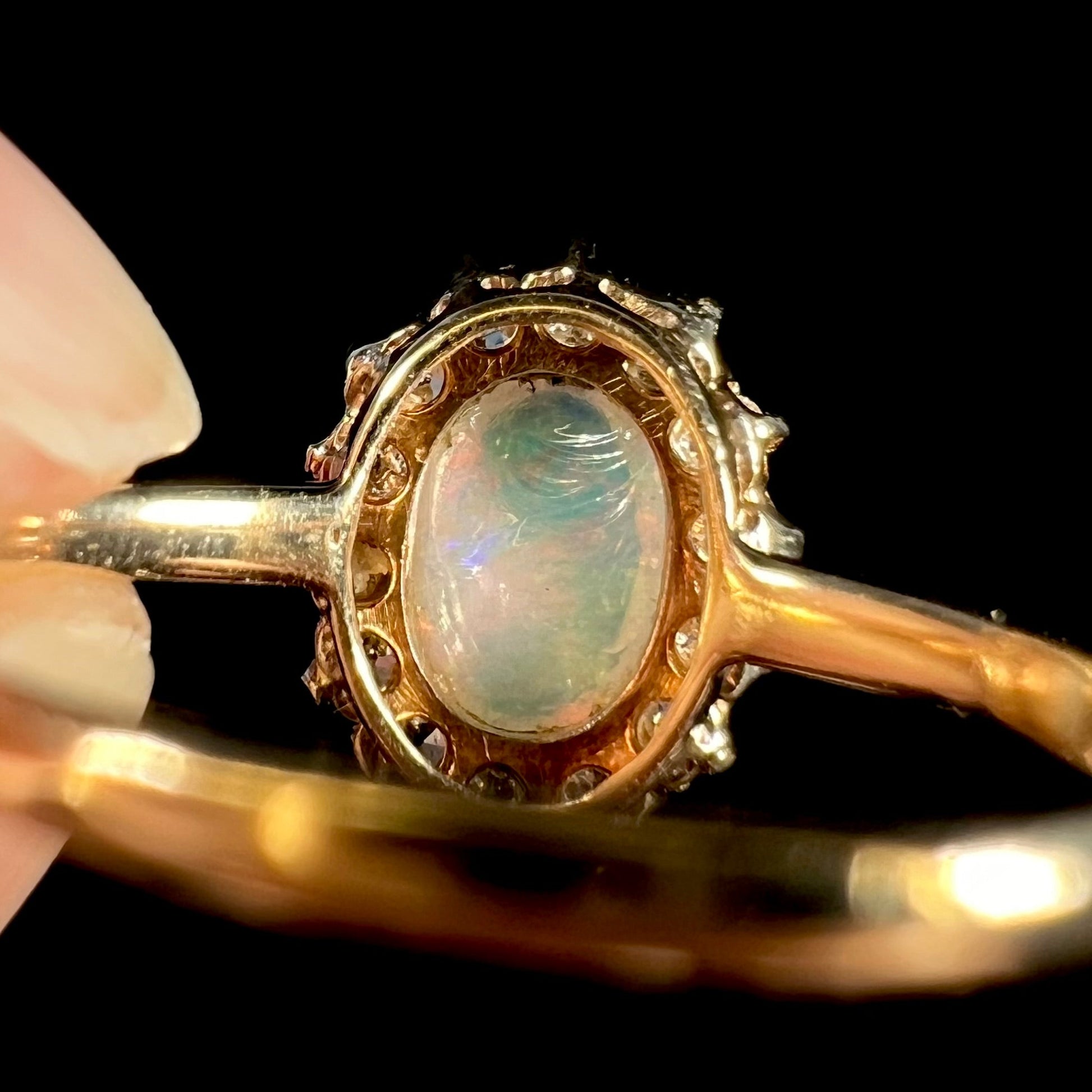 An 18k yellow gold Edwardian style opal and diamond halo ring.  The diamonds are Old European Cut, and the opal shines reddish pink colors.