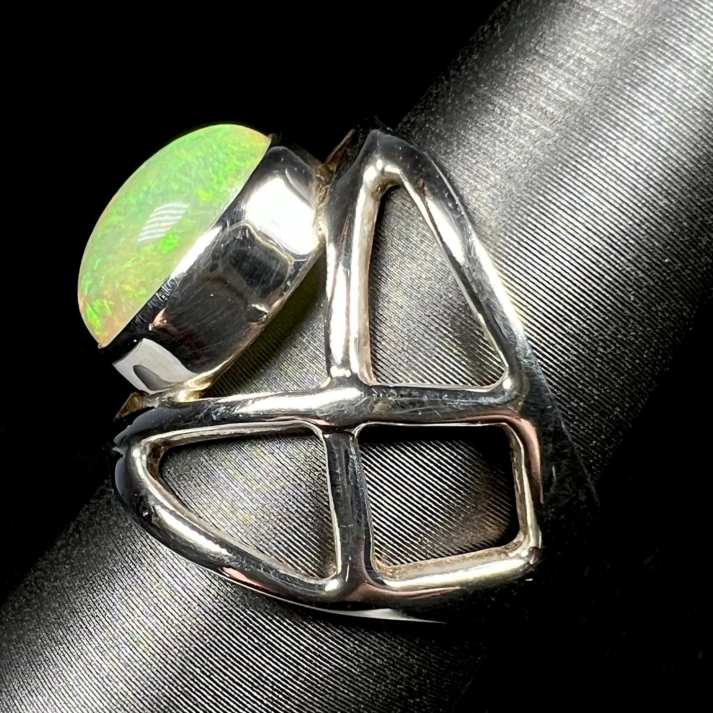 Side view of a silver opal ring with an open design against black backdrop.