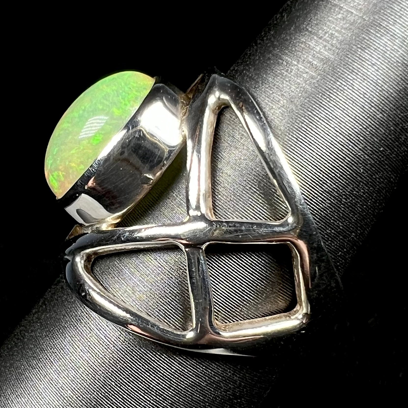 Side view of a silver opal ring with an open design against black backdrop.