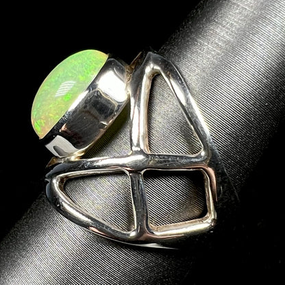 Side view of a silver opal ring with an open design against black backdrop.