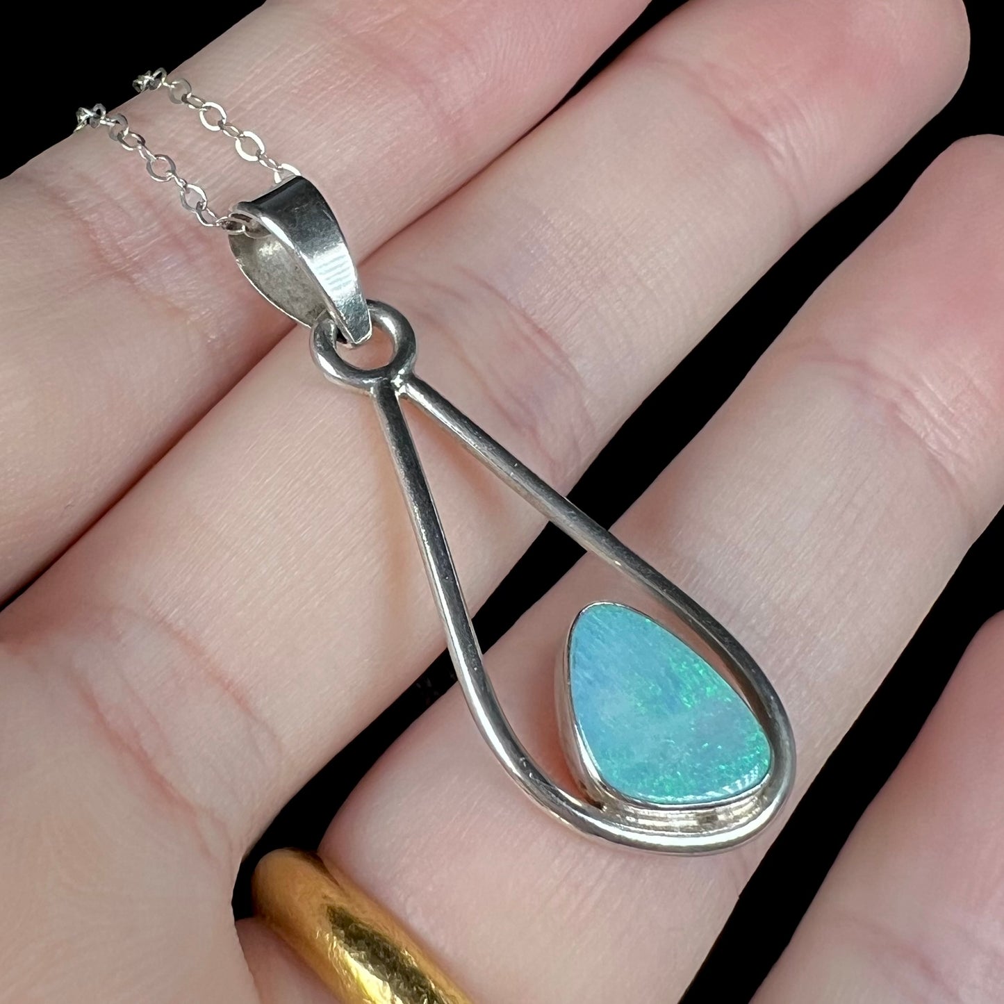 Angled close-up of an open Modernist-style doublet opal pendant in a hand under studio light.