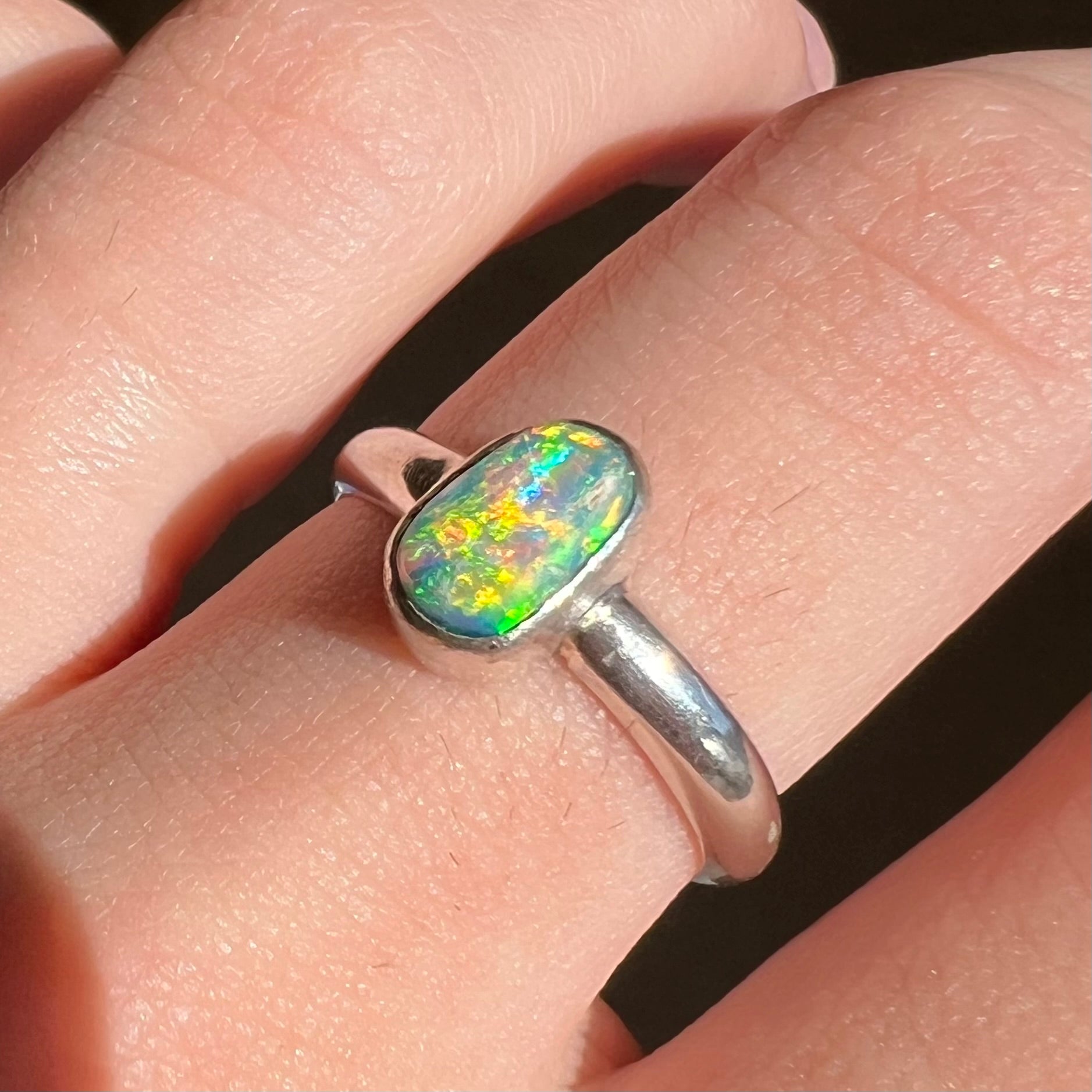 Close-up of orange flashes in Australian crystal opal ring, worn on finger in sunlight