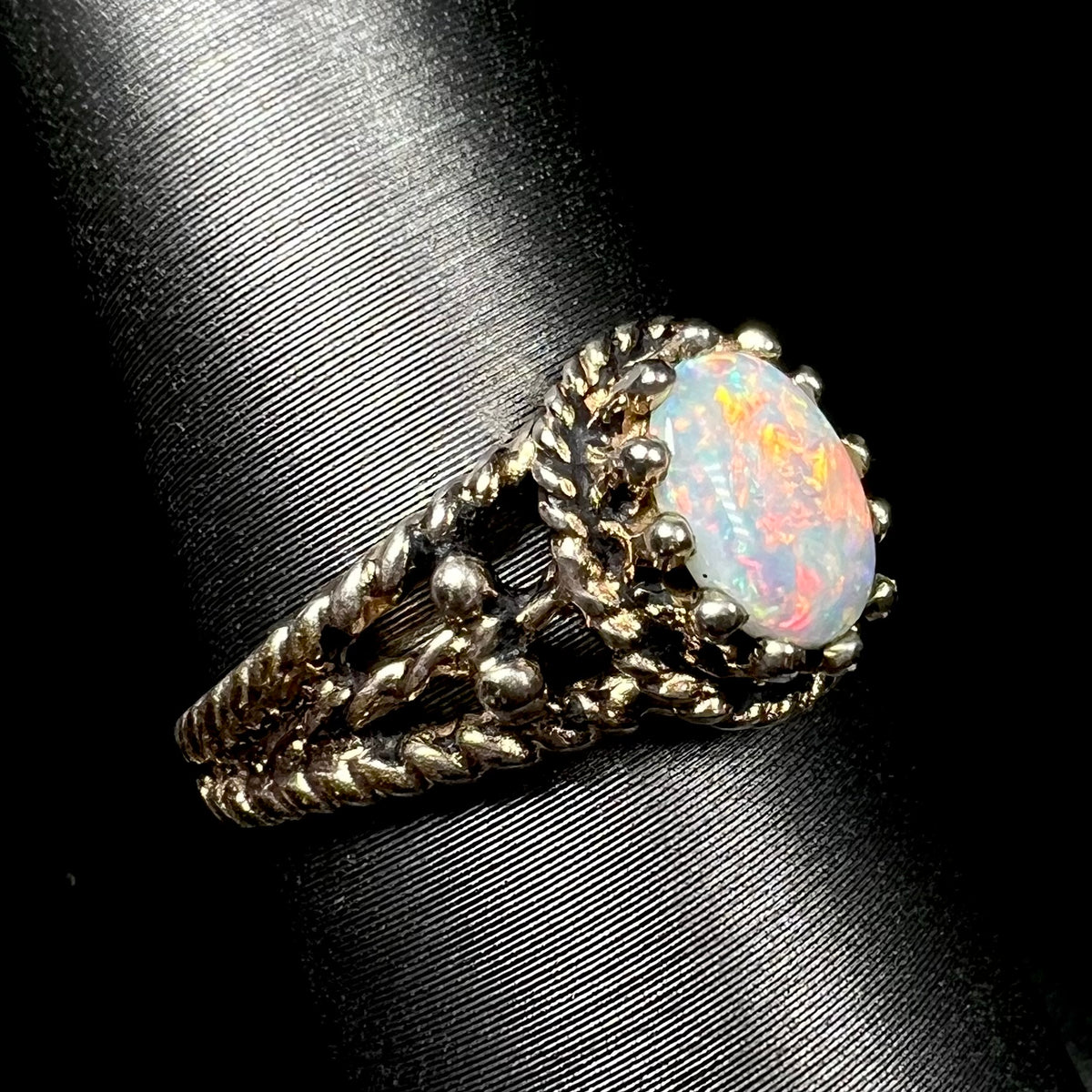 Angled close-up of orange-playing Australian opal ring in base metal with twisted rope design shank, shown on ring display.