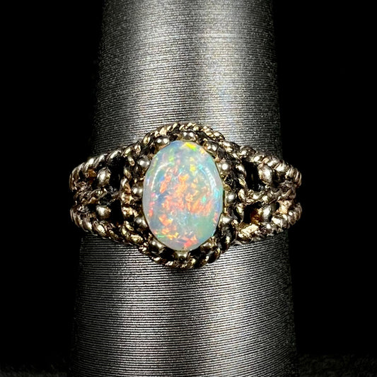 Close-up of estate Australian opal solitaire ring in base metal brass on ring display; the opal has a bright orange flash of color.
