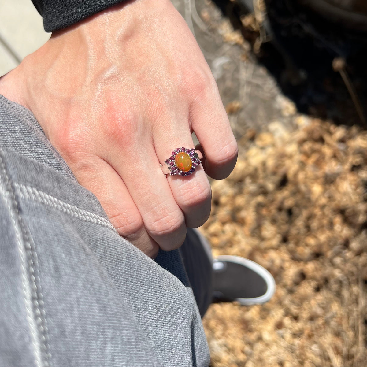 Person's hand resting on hip in sunlight wearing orange Ethiopian opal and garnet ring made from sterling silver