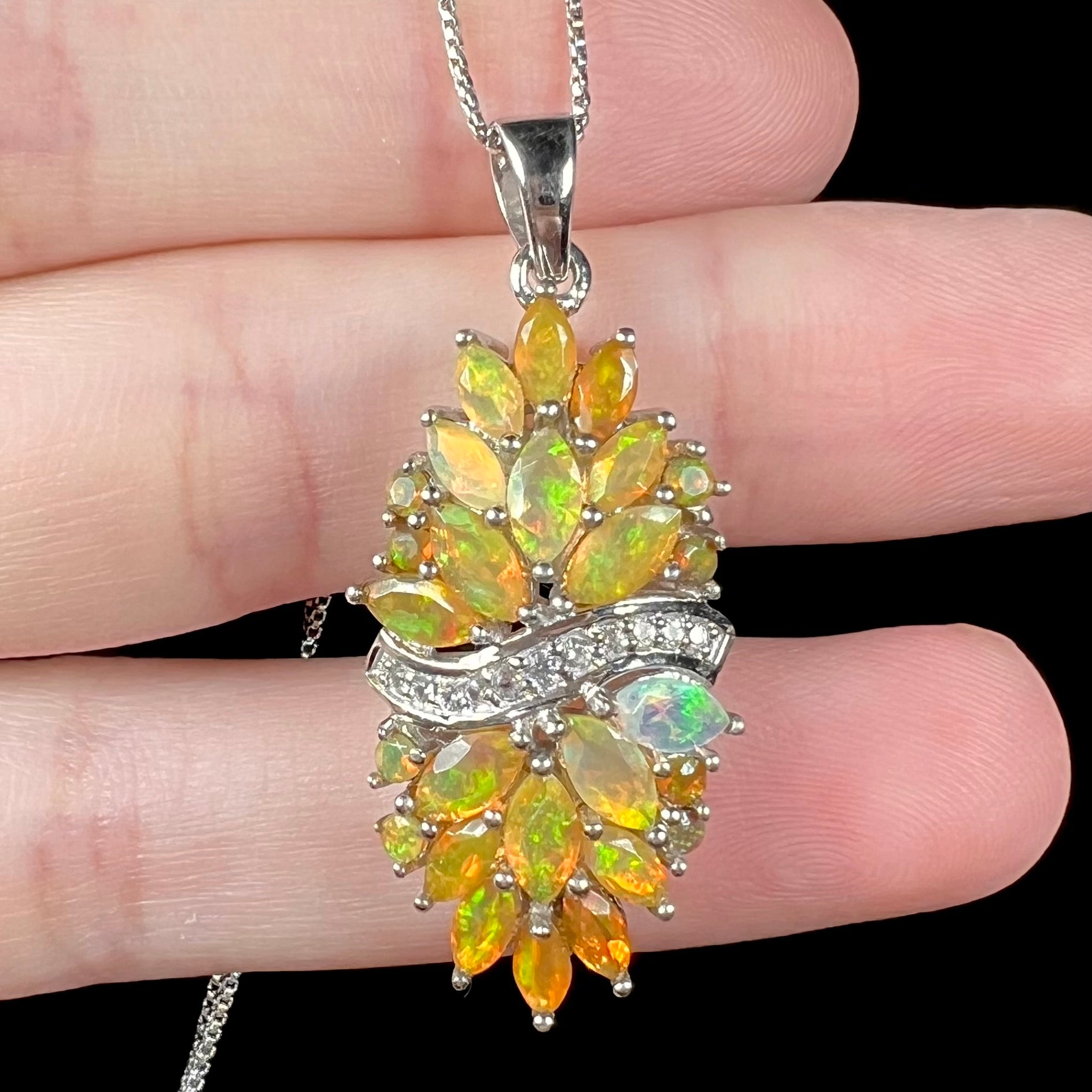 Close-up of a faceted orange fire opal cluster pendant made from sterling silver.  The pendant rests on fingers.