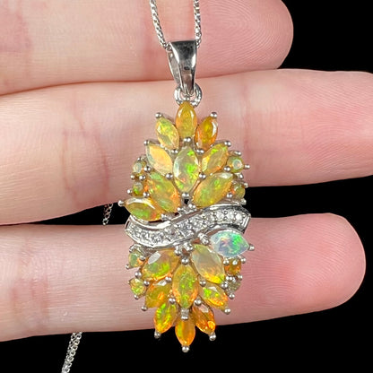Close-up of a faceted orange fire opal cluster pendant made from sterling silver.  The pendant rests on fingers.