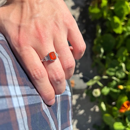 Hand resting on person's hip outdoors in sunlight wearing an emerald cut orange fire opal ring.