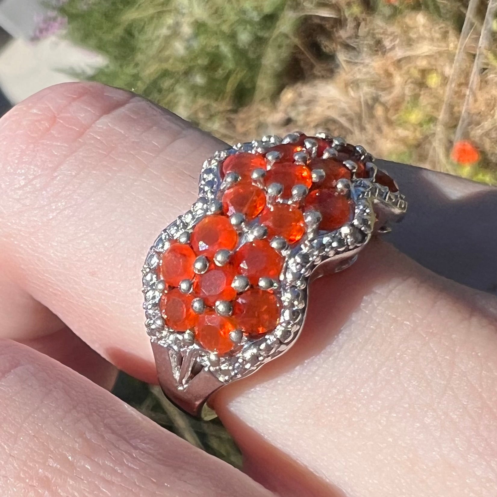 An orange fire opal cluster ring in sterling silver, shown in natural light from an angle while worn on a finger.
